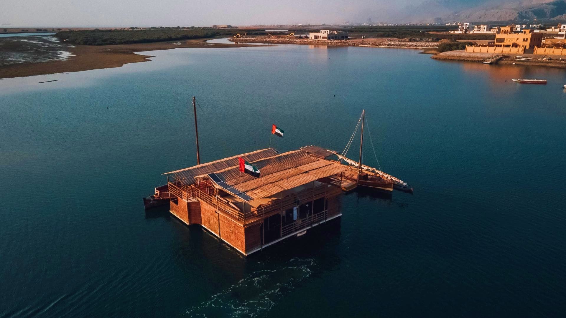 House of Pearls Traditional wooden dhow with UAE flag anchored in turquoise lagoon waters near coastal buildings and mangroves